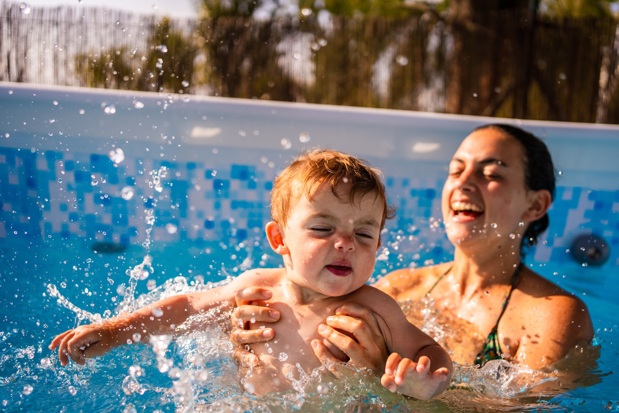 Mother and baby playing and splashing water in a pool house